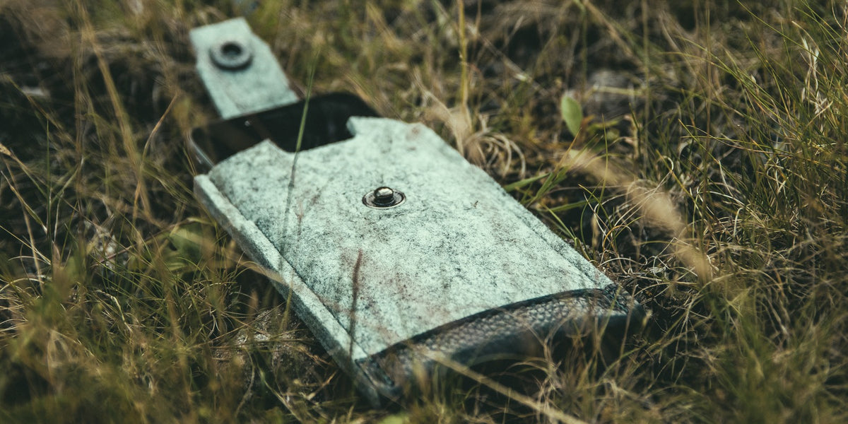 Grey Merino wool felt iPhone sleeve with the popper open, lying in long grass